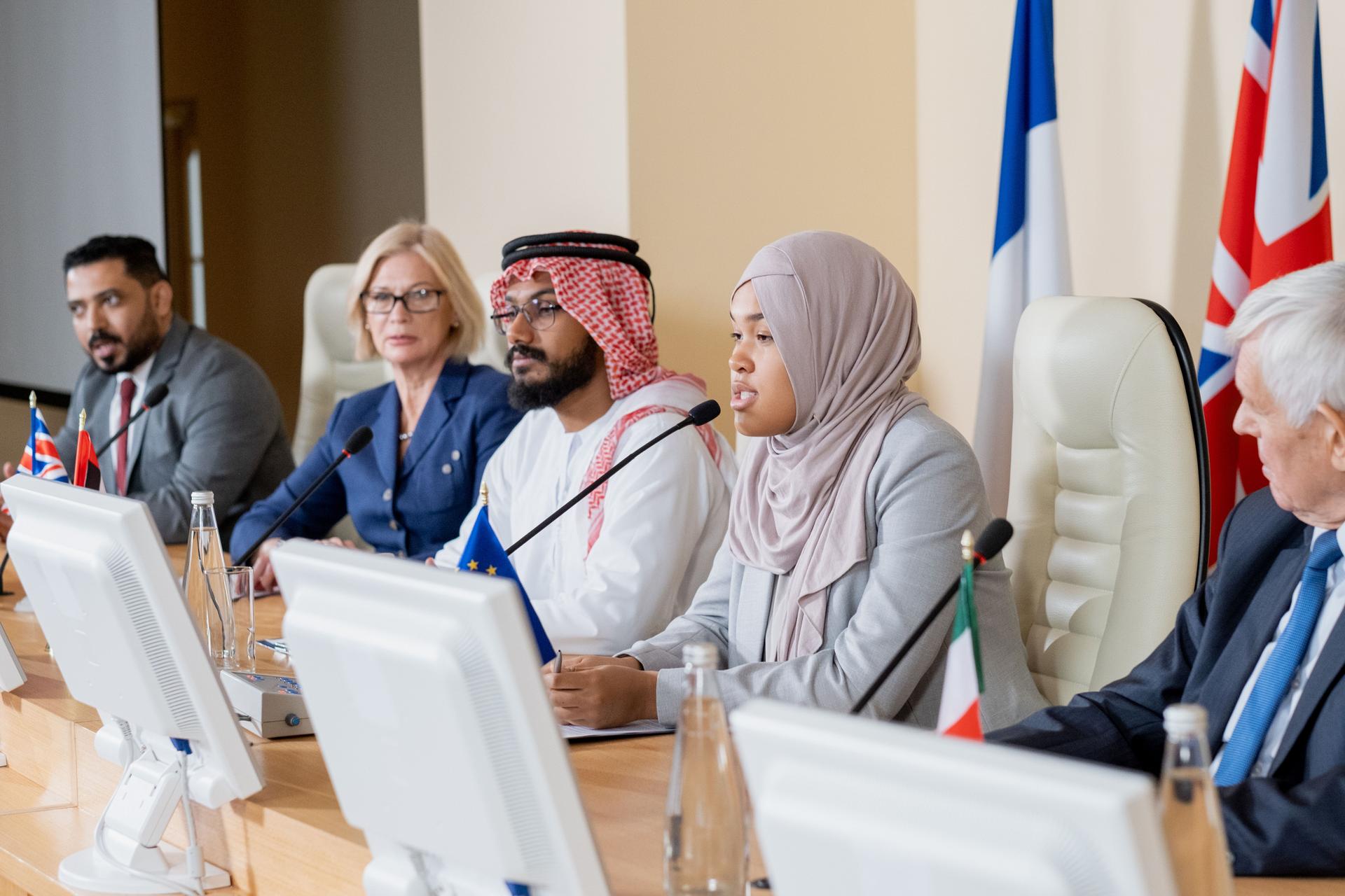 Young Muslim female in hijab making report to foreign colleagues